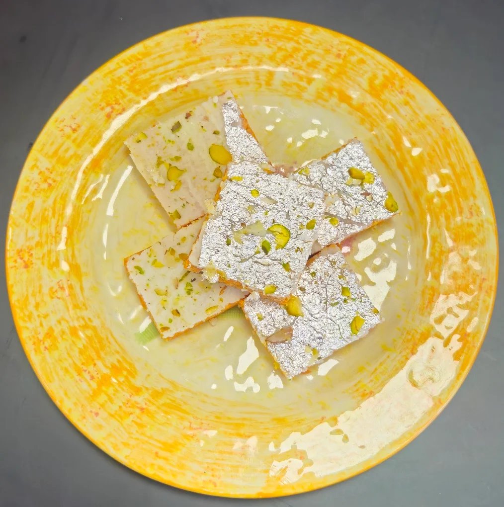 Kaju katli barfi squares with silver leaf and pistachio on a golden plate