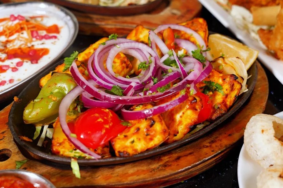Tandoori paneer tikka with red onion and peppers on a sizzling platter