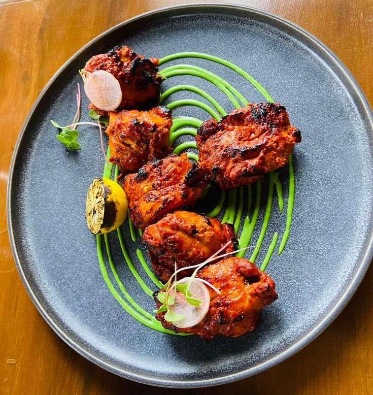 Tandoori chicken on a dark ceramic plate