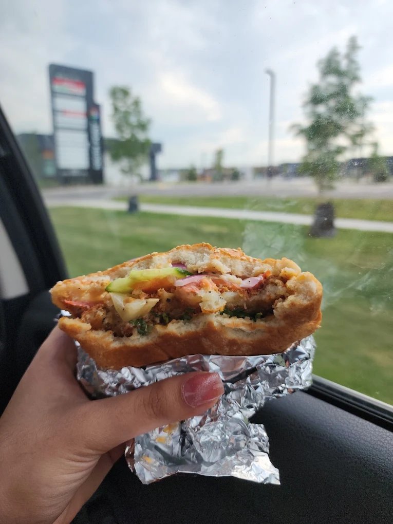Hand holding a loaded crispy chicken sandwich in foil by the food truck